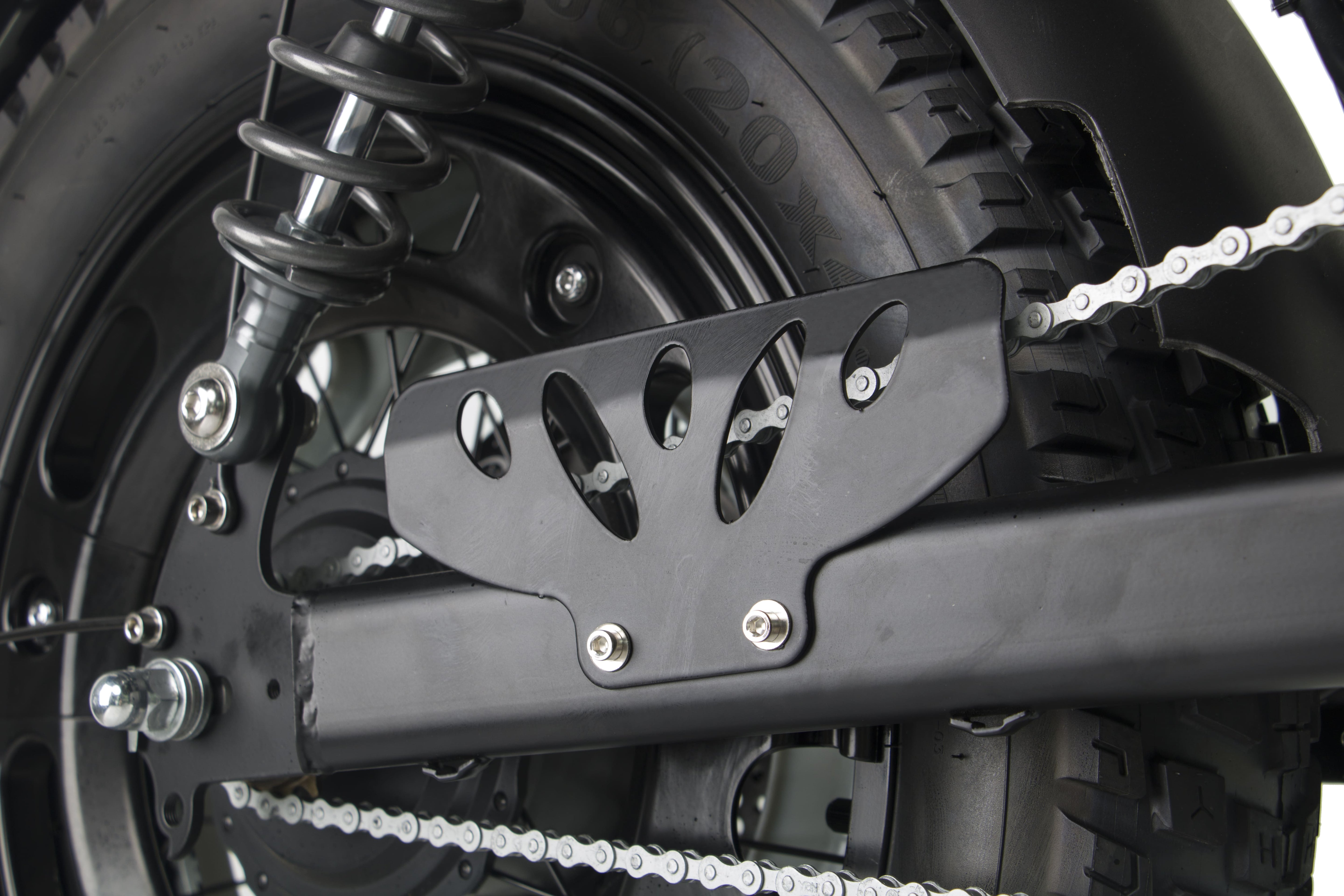Rear chain guard and sprocket area on a black electric motorcycle with knobby tire.